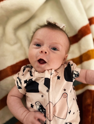Close-up portrait of an infant lying on a blanket and wearing a patterned outfit.