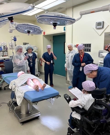 Mannequin on an operating room table surrounded by health care team members in surgical attire.