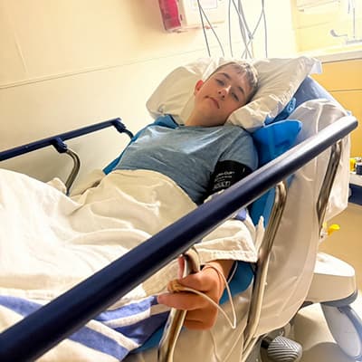 Young person resting in a hospital bed with a blood pressure cuff and monitoring sensor in place.