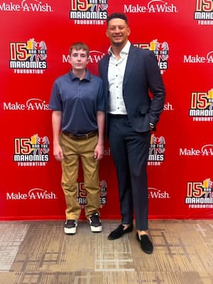 Two people standing in front of a Make-A-Wish and 15 and the Mahomies Foundation event backdrop