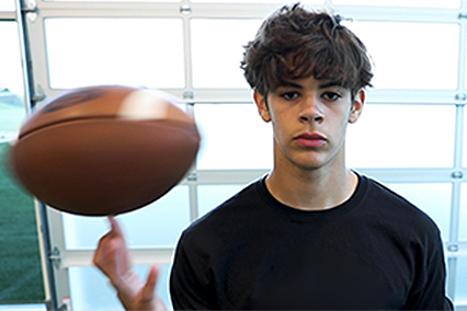 Student athlete spinning a football on one finger while standing in an indoor training or rehabilitation facility.