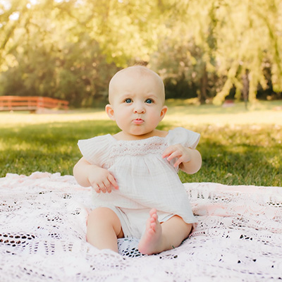 Infant seated on a blanket outdoors in a grassy park setting.