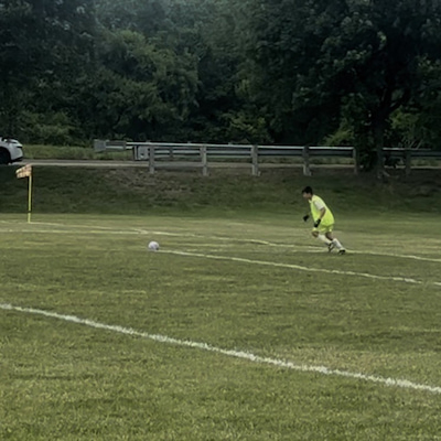 Child in a bright yellow soccer uniform running toward a ball on an outdoor field.