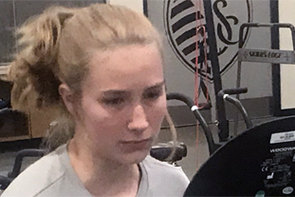 Person exercising on a stationary bicycle in a rehabilitation or performance training facility.