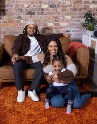 Dad James, Mom Taylor and baby Rose wearing brown toned clothing on a couch 