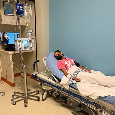 Patient resting on a hospital stretcher while connected to IV infusion equipment and medical monitoring devices.