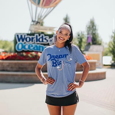 Person standing outdoors in front of a sign, wearing a 'Dream Big' T-shirt.