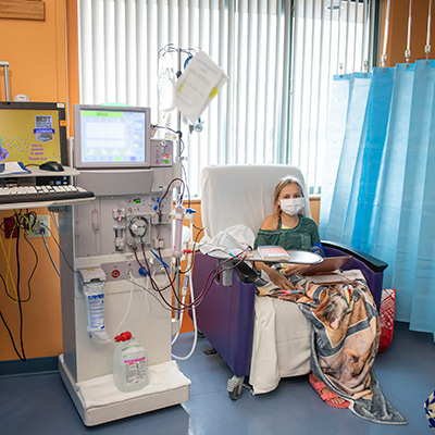 Patient seated in a treatment chair while connected to a dialysis machine in a clinical care room.