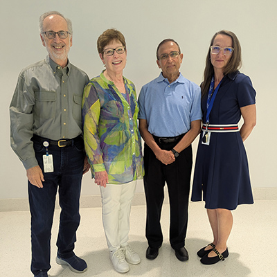 Four adults standing together indoors and posing for a group photo.