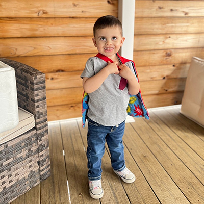 Young child standing on a porch wearing a superhero cape