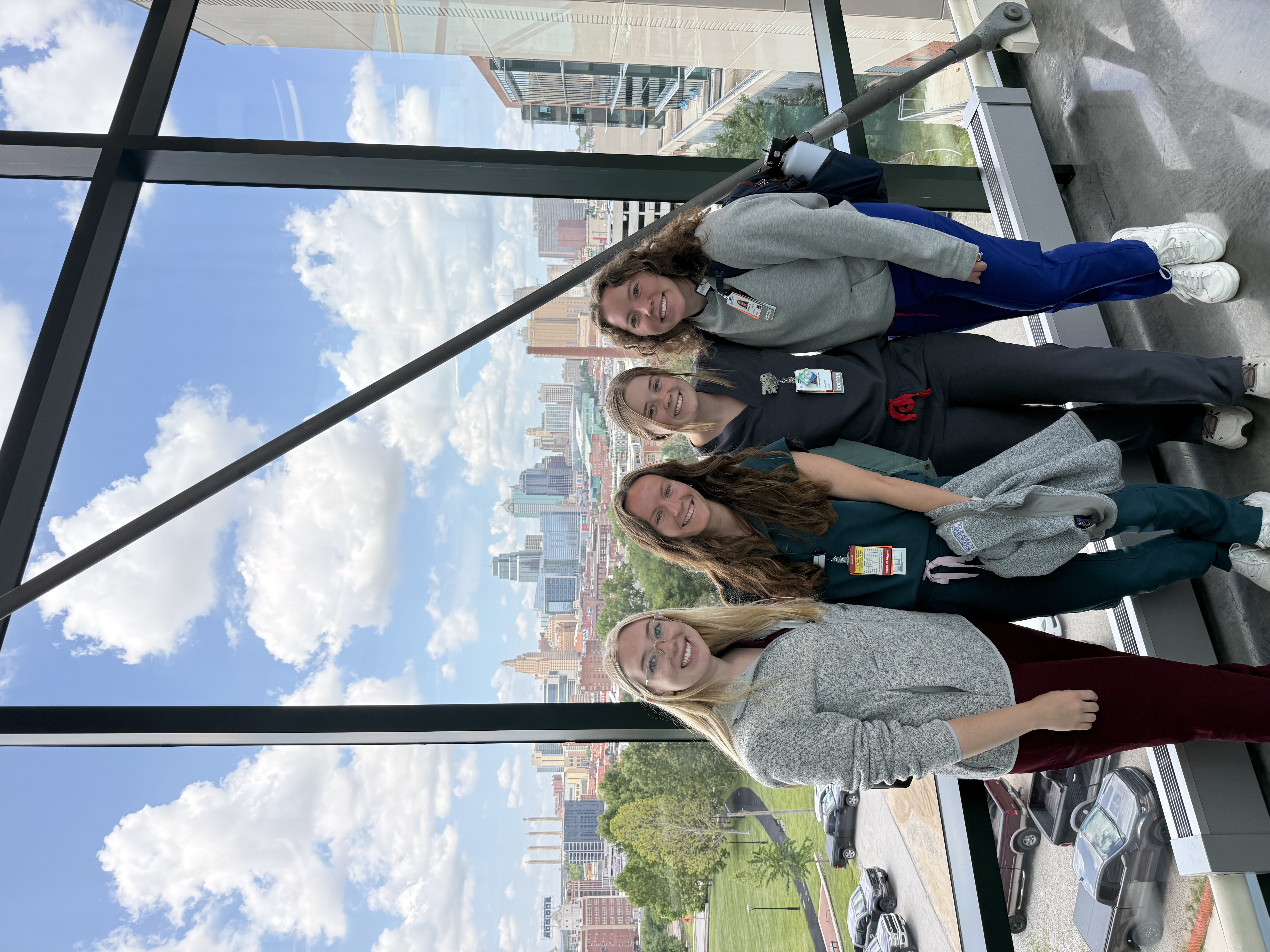 Four Children's Mercy Residents pose in front of a window overlooking the Kansas City skyline.