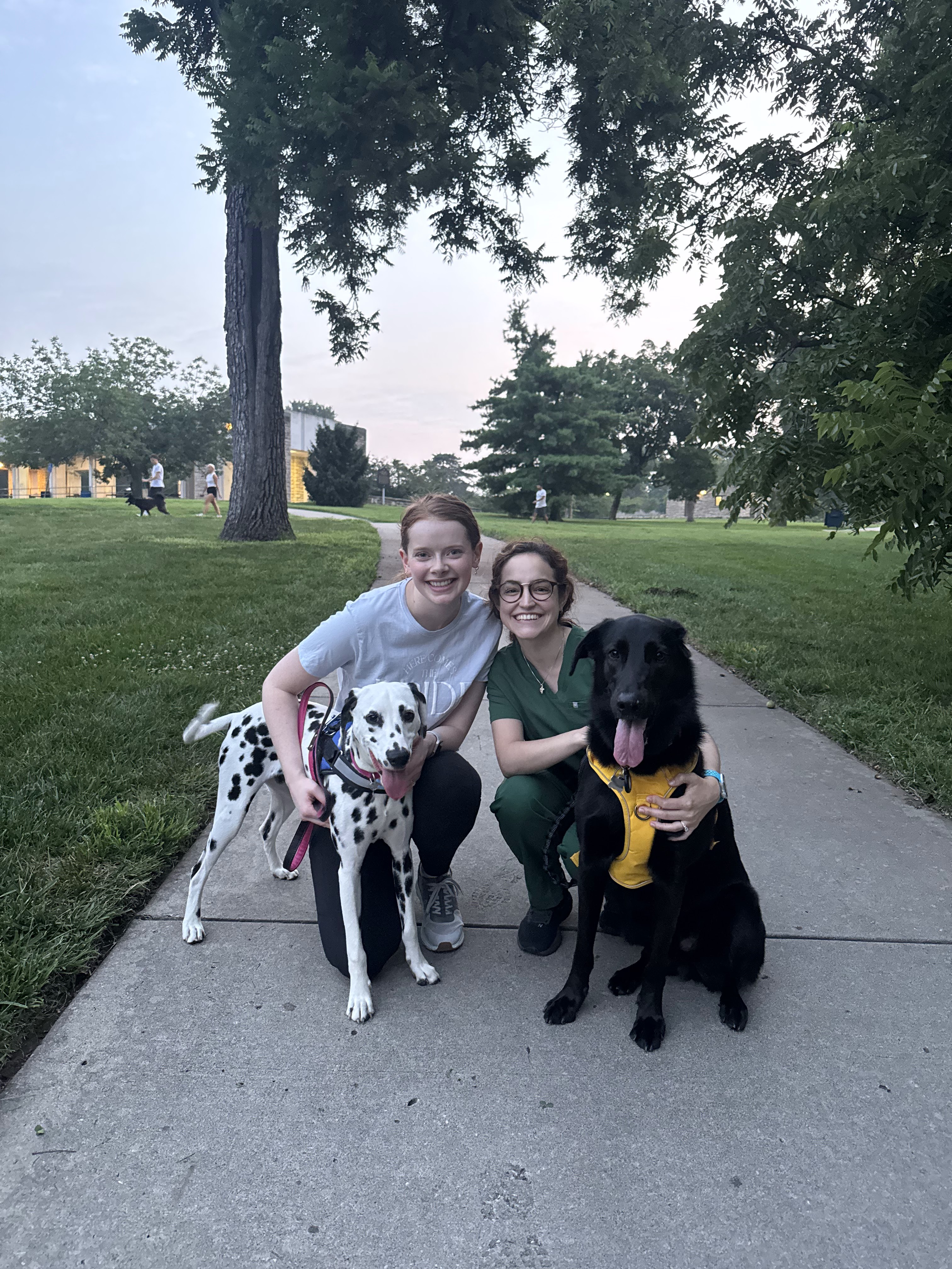 Two Children's Mercy Residents pose with a Dalmatian and a black dog on a park path.