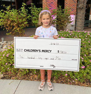 Child holding a ceremonial donation check benefiting Children's Mercy.