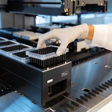 A hand wearing a white glove places a bunch of black tubes held together into a machine. 