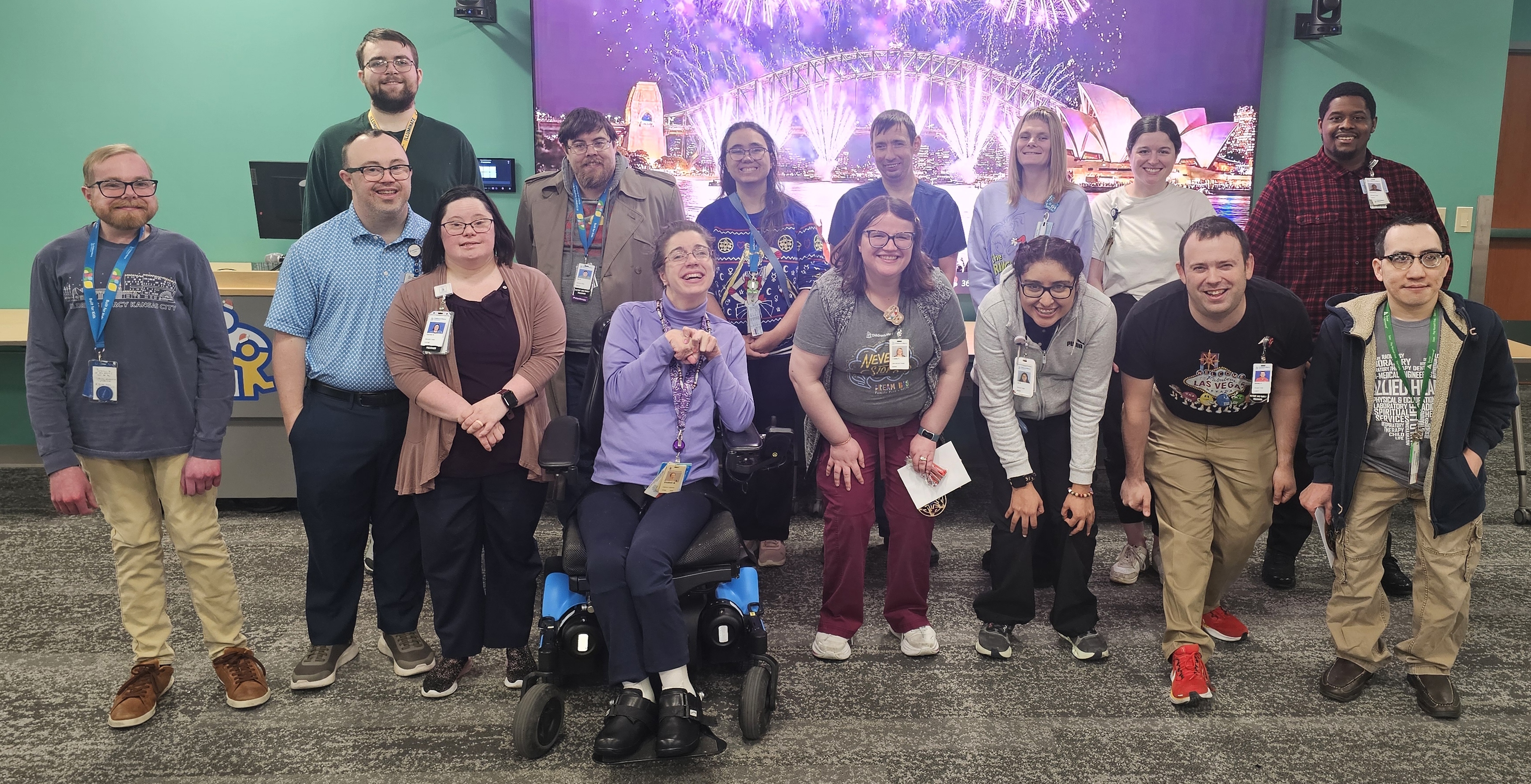 15 members of Project RISE pose together in a room with carpet and a teal green wall behind them. They are a mix of men and women.