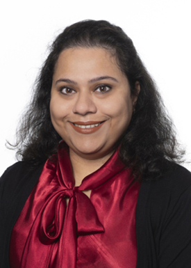 A portrait of Dr. Dithi Banerjee on a white background. She has long dark hair and is wearing a deep red blouse with a black cardigan over it.