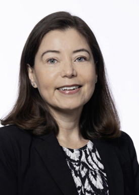 A portrait of Dr. Susana Chavez-Bueno. She has brain hair that falls to her shoulders and is wearing a black blazer with a white and black shirt underneath it.