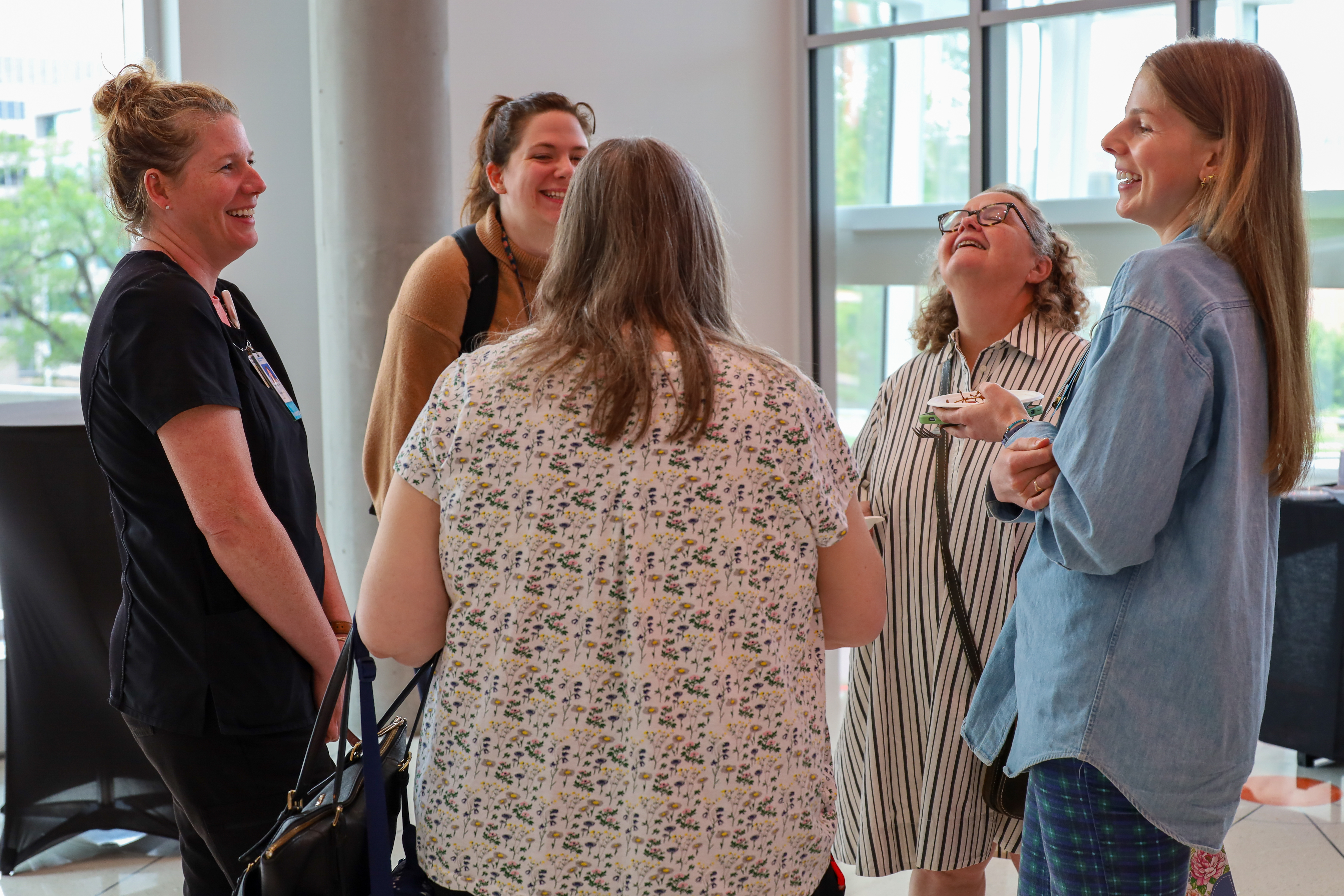 Five women stand in a circle laughing with one another. 