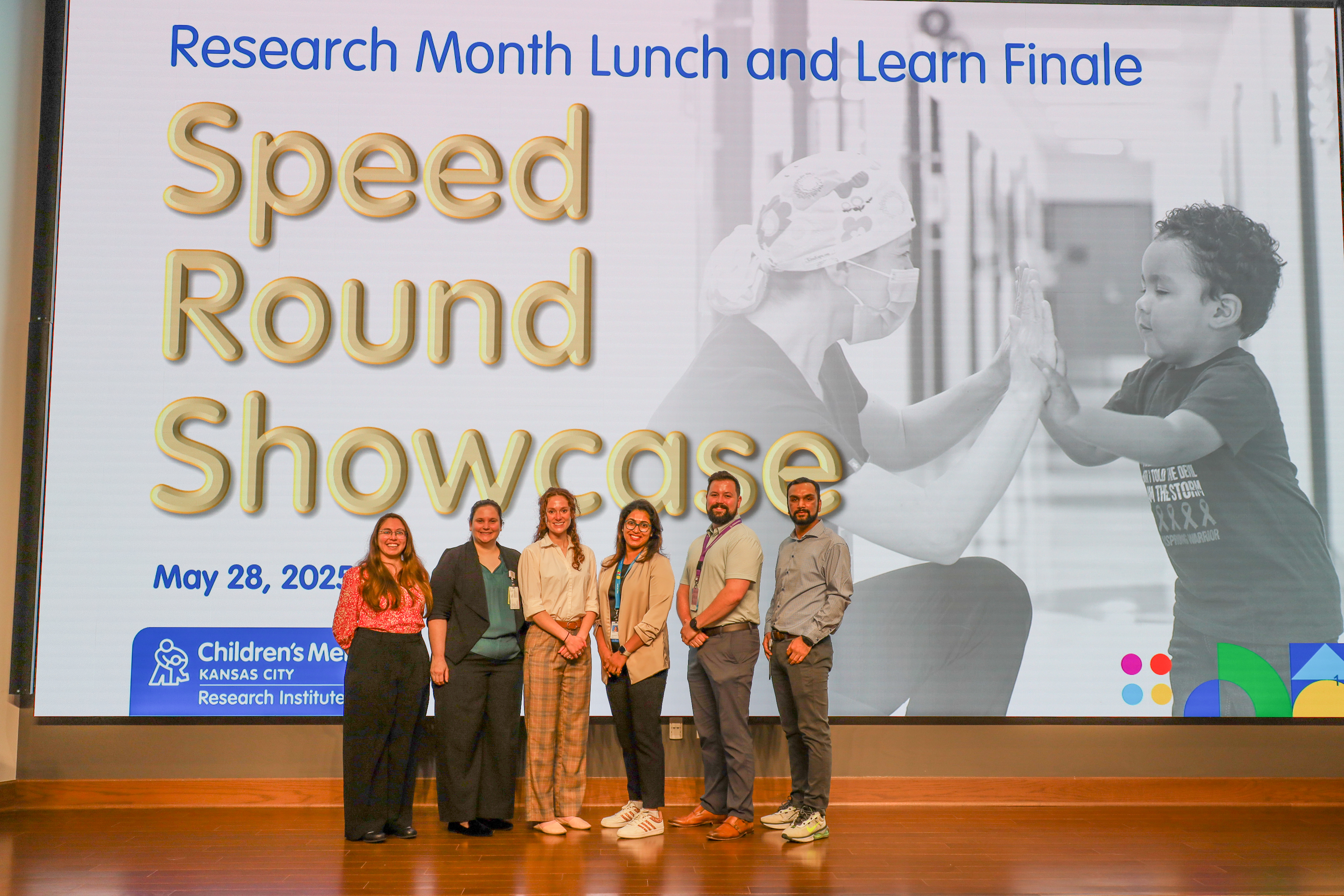 Six people stand on stage together, 4 women and 2 men. Behind them is a big screen that says Speed Round Showcase.