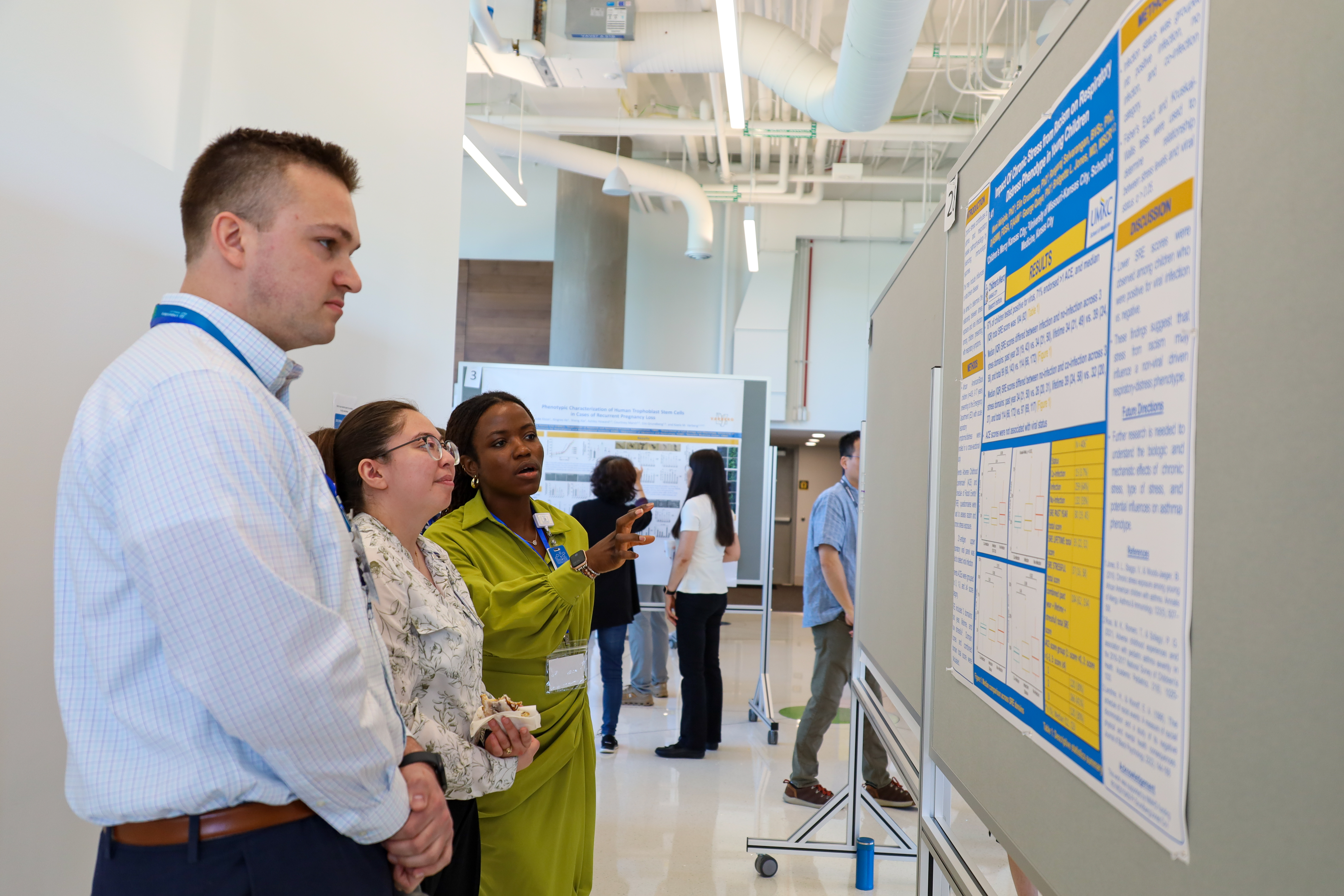 A man and a woman stand looking at a research poster while another woman motions to something on the poster while talking.