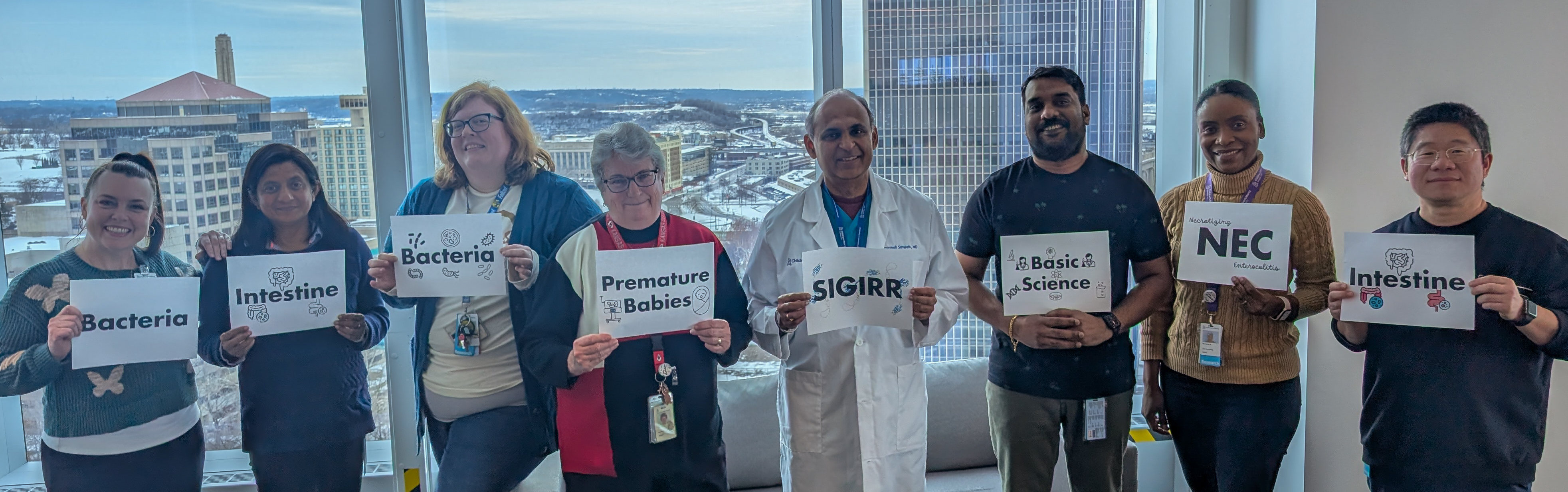 Dr. Sampath and his lab team (7 people) hold up signs of keywords that are integral ideas held within a 2025 NIH grant he received. They are words like Bacteria, Intestine, and SIGIRR. 