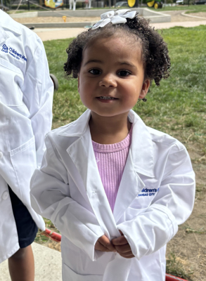 A young girl stands outside wearing a lab coat.