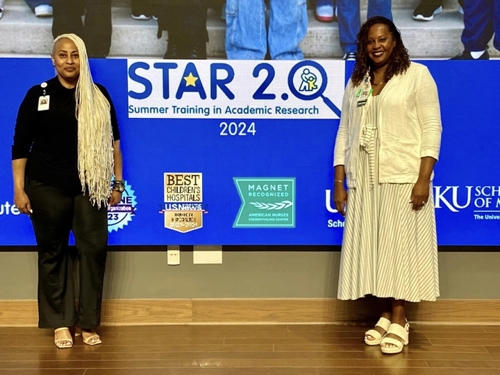 Two women stand on stage. with a screen behind them that says STAR 2.0 Summer Training in Academic Research. 