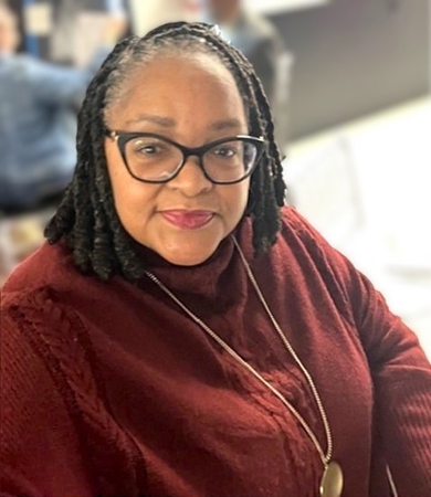 Darlene Brenson Hughes. She has black hair and is wearing glasses. She is wearing a maroon long-sleeve shirt.