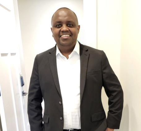 Freddie Karumbi. He is wearing a dark colored blazer with a white shirt underneath. 