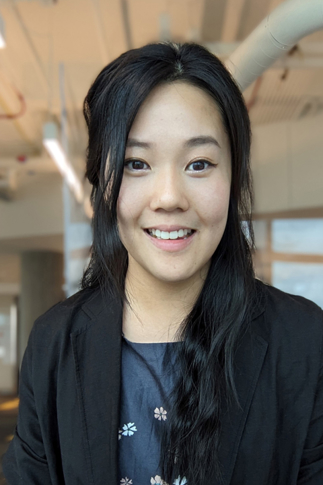 Wendy Wang. Her dark, long hair is half pulled up. She wears a black blazer with a blue shirt underneath that has flowers on it.