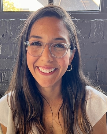 Xiomara Aguilera. She has long brown hair and is wearing glasses. She's wearing a white shirt and a necklace.