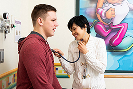 Health care team member using a stethoscope to listen to a patient's chest during an exam in a pediatric clinic room