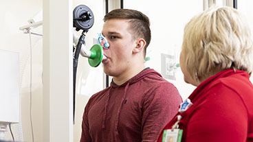 Patient using a spirometer during a pulmonary function test as a health care team member monitors the assessment