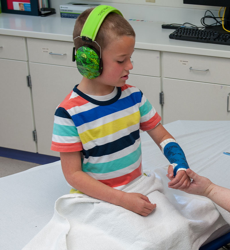 image of a child sitting on a bed with headphones with a cast on their arm