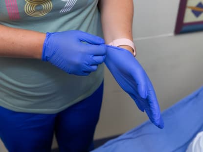 hands of a nurse putting gloves on that are blue. 